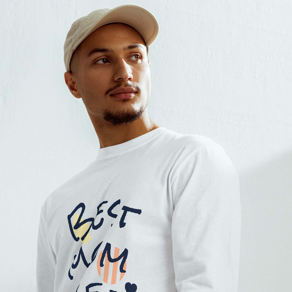 Model wearing a heavyweight long sleeve shirt with graphic design and beige cap, showcasing premium garment-dyed cotton.